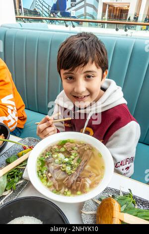 Ein Junge isst eine Schüssel Pho, eine vietnamesische Suppe mit Rinderbrust, Nudeln und Frühlingszwiebeln. Stockfoto