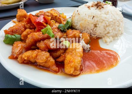 Ein Teller mit süßem und saurem Hühnchen mit gekochtem Reis, ein chinesisch inspiriertes Essen, das in einem britischen Food Court serviert wird. Stockfoto