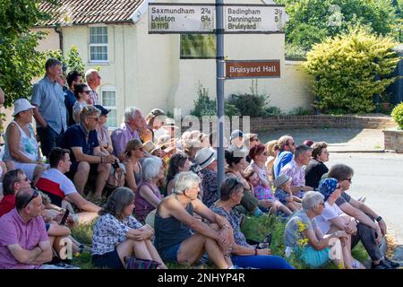 An einem sonnigen Sonntag sitzen die Dorfbewohner am Grasrand, um den Rendham Mummers beim Feiern der Sommersonnenwende mit einer Show über die Römer und die Iceni zuzusehen Stockfoto