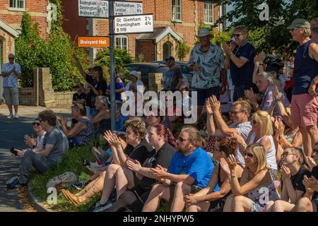 An einem sonnigen Sonntag sitzen die Dorfbewohner am Grasrand, um den Rendham Mummers beim Feiern der Sommersonnenwende mit einer Show über die Römer und die Iceni zuzusehen Stockfoto