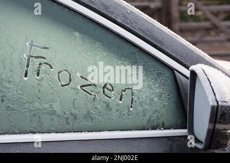Harter Frost und Temperaturen unter Null lassen Sie die Windschutzscheibe des Fahrzeugs mit einer Schicht Frosteis bedeckt, die vor der Fahrt entfernt werden muss. Meldung „kalt gefroren“ Stockfoto