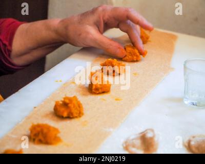 Seniorin bereitet gefüllte Kürbis-Ravioli-Tortelli mit italienischem Vollkornmehl zu Hause zu, hausgemachtes Essenskonzept Stockfoto