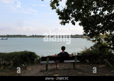 13-jähriger Junge, der auf einer Bank saß und von der Promenade Paul Chapel auf der Pointe des emigres im Parc du Golfe, Vannes, Stockfoto