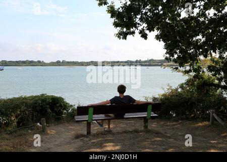 13-jähriger Junge, der auf einer Bank saß und von der Promenade Paul Chapel auf der Pointe des emigres im Parc du Golfe, Vannes, Stockfoto