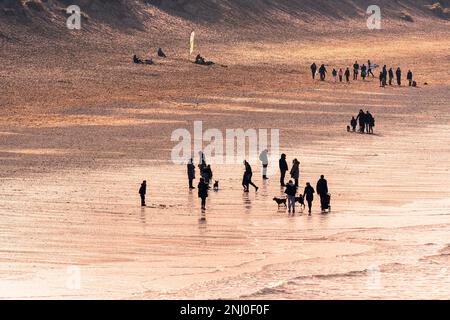 Abendlicht, das Menschen am Fistral Beach bei Ebbe in Newquay in Cornwall in Großbritannien umhüllt. Stockfoto