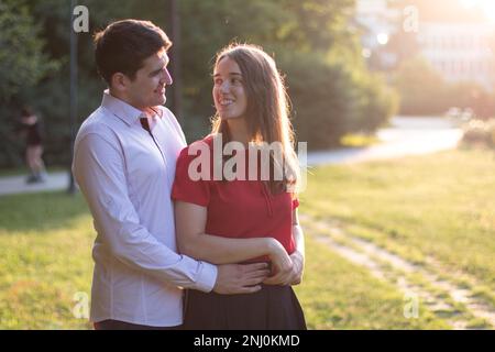 Ein verliebtes junges Paar, das Zeit miteinander im Park verbringt, der Mann umarmt die Frau von hinten. Stockfoto