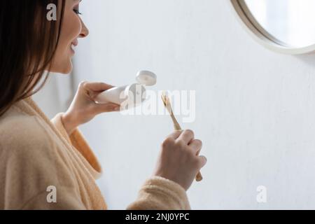 Glückliche junge Frau, die morgens eine Tube mit Zahnpasta und Zahnbürste hielt, Stockbild Stockfoto