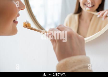 Kurzer Blick auf eine junge und glückliche Frau, die in der Nähe des Spiegels im Badezimmer Zähne putzt, Stockbild Stockfoto