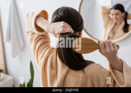 Rückansicht einer jungen brünetten Frau, die im Badezimmer Haare bürstet, Stockbild Stockfoto