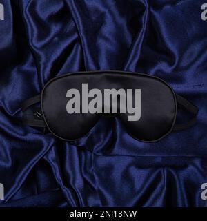 Schwarze Seidenmaske liegt auf dunkelblauem Seidenhintergrund. Draufsicht. Quadratische Ausrichtung Stockfoto