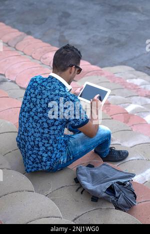 Ein rückwärtiges Bild eines jungen Mannes, der mit einem Tablet auf einer Tribüne sitzt Stockfoto