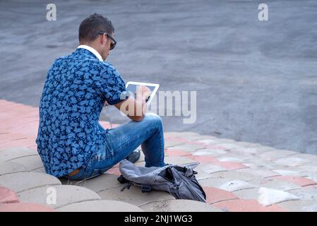 Ein rückwärtiges Bild eines jungen Mannes, der mit einem Tablet auf einer Tribüne sitzt Stockfoto