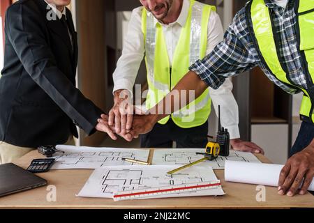 Architekturteam, das Hände stapelt und zusammenarbeitet. Bauplan, Bauingenieur, der ein Bauprojekt skizziert. Stockfoto