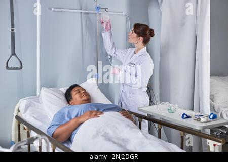 Porträt einer jungen Krankenschwester, die eine IV-Therapie für Seniorin im Krankenhausbett einrichtet Stockfoto
