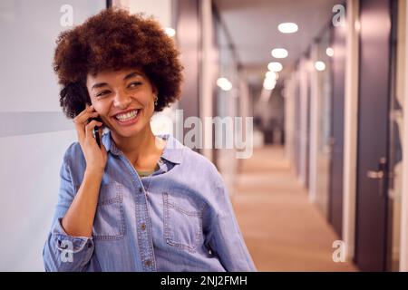 Lächelnde Junge Geschäftsfrau Im Korridor Des Modernen Büros, Die Am Telefon Spricht Stockfoto