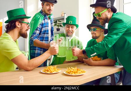 Eine Gruppe männlicher Freunde, die Patrick's Day feiern, Becher klimpern und grünes Bier trinken Stockfoto