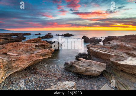 Atemberaubender Sonnenaufgang über dem Strand und Felsen am Torre de la Sal in der spanischen Region Valencia Stockfoto