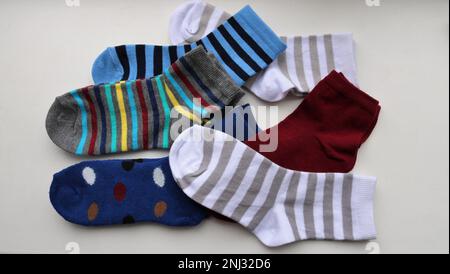 Stilleben von mehrfarbigen Baumwollsocken für Kinder, die zufällig auf einer leichten Oberfläche liegen, eine chaotische Anordnung von Kleidungsstücken für Kinder, neue kleine Socken Stockfoto