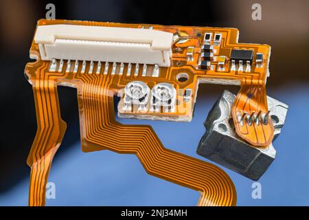 Orangefarbene Leiterplatte mit flexiblen Flachbandkabeln, kleinen elektronischen Bauteilen und weißem Steckverbinder. Leiterplatte im optischen CD/DVD-Laufwerk. Stockfoto