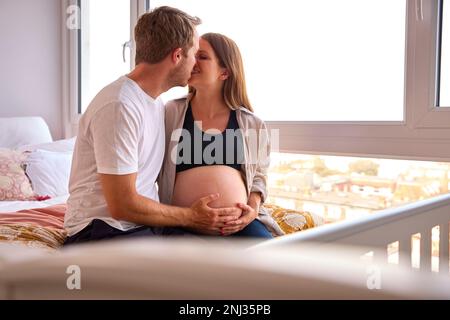 Ein liebevolles Paar zu Hause, das mit einem Mann im Bett sitzt, der den Magen einer schwangeren Frau berührt Stockfoto
