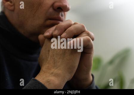 Besorgter religiöser Seniorist betet mit erhobenen Händen zu gott und rührt sich, während er um Hilfe und Inspiration betörend in den Himmel schaut. Stockfoto