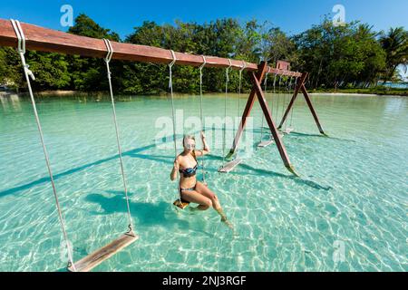 Wunderschöne weibliche Touristen, die sich auf einer Schaukel in Laguna Bacalar in Mexiko während des Kajakausflugs entspannen. Stockfoto