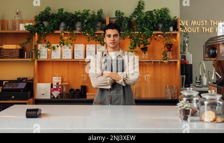 Ein junger selbstbewusster Barista, der beim Stehen an der Theke gerade in die Kamera schaut Stockfoto