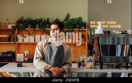 Selbstbewusster, lokaler Coffee Shop-Besitzer, der eine Schürze trägt. Männlicher Barista, der in einem Café wegschaut. Stockfoto
