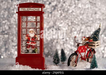 Der Weihnachtsmann in der Telefonzelle, mit dem Fahrrad des Weihnachtsmanns im silbernen Holz. Weihnachtsdekoration Stockfoto