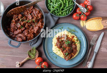 Schweineeintopf mit cremigen Polenta und grünen Bohnen. Köstliches glutenfreies fleisch am sonntag oder an Feiertagen Stockfoto