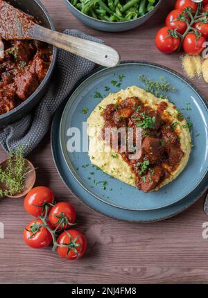 Schweineeintopf mit cremigen Polenta und grünen Bohnen auf einem Holztisch. Köstliches sonntag- oder Feiertagsessen oder Mittagessen Stockfoto