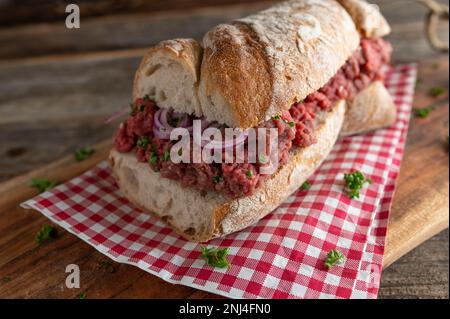 Rohes Rindfleisch-Sandwich mit roten Zwiebeln, Petersilie auf rustikalem, französischem Baguette Stockfoto