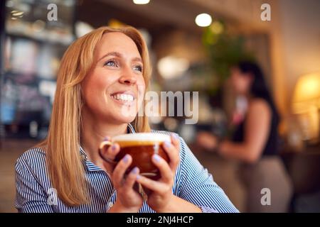 Lächelnde Frau, Die An Einem Tisch Im Café Sitzt Und Ein Heißes Getränk Genießt Stockfoto