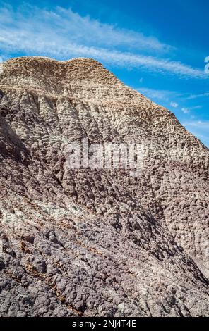 Ein steiler, gefurchter grauer und violetter Lehmgipfel mit einem blassen Gipfel erhebt sich vor einem blauen Himmel, Petrified Forest National Park, Arizona. Stockfoto