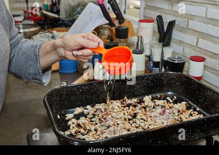 Kochen gießt Öl in Pilze mit Zwiebeln in der quadratischen Bratpfanne. Stockfoto