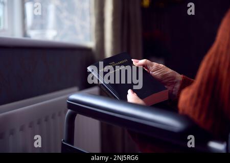 Seniorin Im Rollstuhl Mit Bibel, Die Sich In Der "Cost Of Living" -Krise Durch Heizkörper Zu Hause Warm Hält Stockfoto