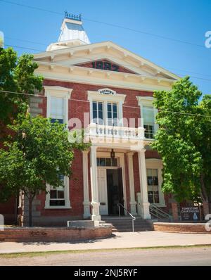 Das rote Backstein-Gerichtsgebäude von Tombstone hat eine weiße Säulenveranda, einen Balkon und eine Kuppel, eingerahmt von grünen Bäumen unter blauem Himmel in Tombstone, Arizona. Stockfoto