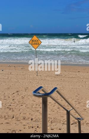 504 Manly Beach wegen schlechter Seebedingungen geschlossen - gelber Schild und weißes Rettungsschwimmbrett - Handlauf aus Edelstahl. Sydney-Australien. Stockfoto