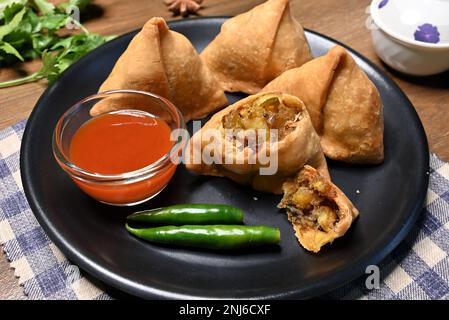 Bild von Samosa oder Singara, ein knuspriger und würziger dreieckiger Snack mit einer herzhaften Füllung aus Kartoffelpüree, Erbsen und Gewürzen, serviert in einer schwarzen Platte Stockfoto