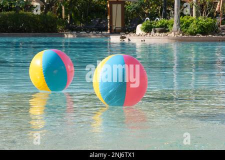 An einem Sommertag schweben zwei bunte Strandbälle im Wasser eines Resortpools. Stockfoto