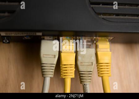 Nahaufnahme einiger mehrfarbiger RJ45-ethernet-Kabel, die an einen schwarzen Router auf einem Holztisch angeschlossen sind Stockfoto