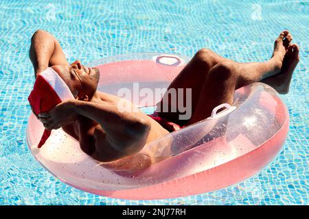 Ein Mann In Den Weihnachtsferien Schwimmt Auf Einem Aufblasbaren Schwimmbecken Und Trägt Einen Weihnachtsmann Stockfoto