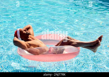 Ein Mann In Den Weihnachtsferien Schwimmt Auf Einem Aufblasbaren Schwimmbecken Und Trägt Einen Weihnachtsmann Stockfoto