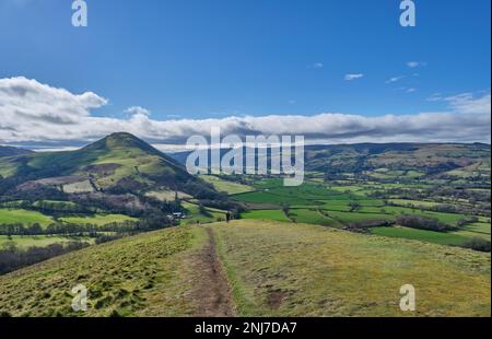 Wanderer steigen vom Gipfel des Lawley in Richtung Comley ab, mit Little Caradoc und Caer Caradoc und dem Long Mynd, nahe Church Stretton, S. Stockfoto