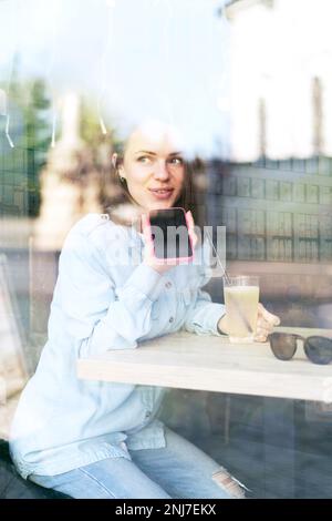 Junge Frau aus der Stadt, die im Café sitzt und Sprachnachrichten mit ihrem Handy aufnimmt. Stockfoto