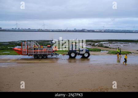 New Brighton Rettungsboot-Crew holt das Boot wieder am Strand ab, wobei der Traktor die Rippe auf einem Anhänger zieht, nachdem er eine Rettung auf dem Meer abgeschlossen hat Stockfoto