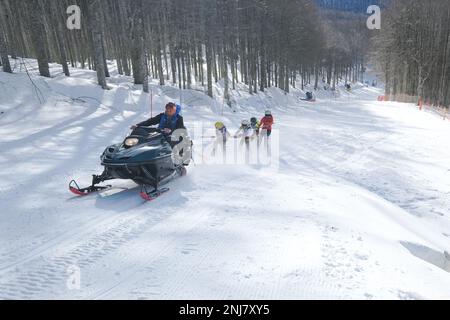 Skifahrer, die von einer kostenlosen Ski-doo-Schneemobilfahrt, Mount Amiata, Toskana, Italien, abgeschleppt werden Stockfoto