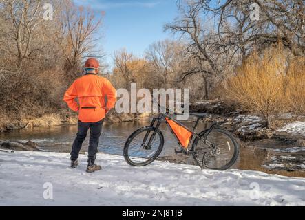 Reife männliche Radfahrer mit einem Mountainbike am Flussufer in der Winterlandschaft: Big Thompson River in Loveland, Colorado Stockfoto