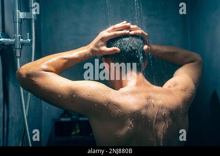 Mann unter der Dusche, der Haare mit Shampoo-Produkt unter Wasser wäscht, das vom luxuriösen Regenduschkopf fällt Stockfoto