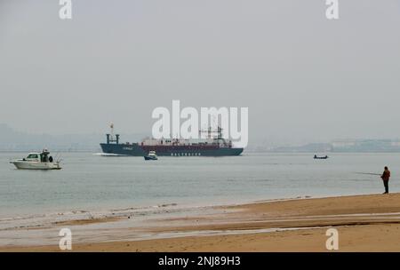 Ein Mann, der vom Strand aus angeln kann, als Cemvale Cement Carrier Frachtschiff, das den Hafen von Santander an einem ruhigen, nebligen Wintermorgen Santander Cantabria Spanien verlässt Stockfoto